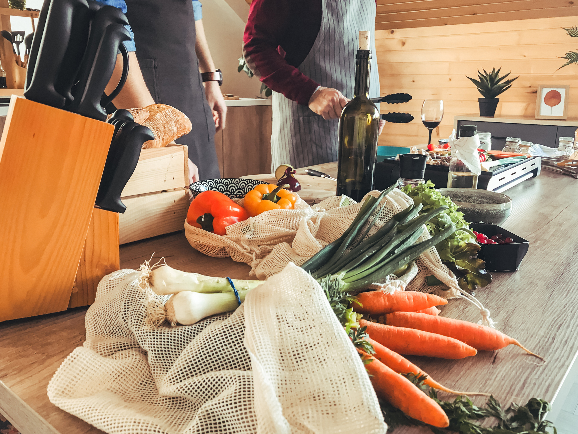 Table full of vegetables and two two men cooking in the background.