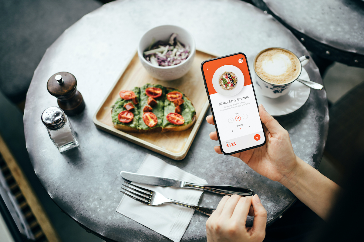 Overhead view of young Asian woman using mobile app device on smartphone to place a food order in a restaurant