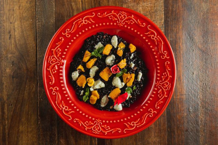 Arroz negro caldoso, cozido no caldo de legumes, banana maçaricada, fonduta de queijo e manjericão / Divulgação