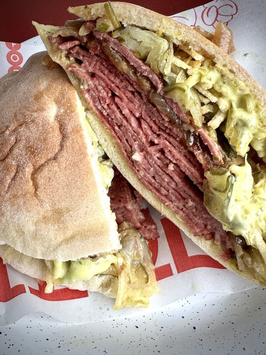 Sanduíche Vursht feito com salame bovino tradicional judaico, molho mostarda, picles de pepino, batata palha da casa chimichurri e cebola caramelizada / Tina Bini