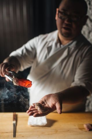 Chef Miyano com binchotan em uma mão e uma peça de niguiri em outra  / Nani Rodrigues