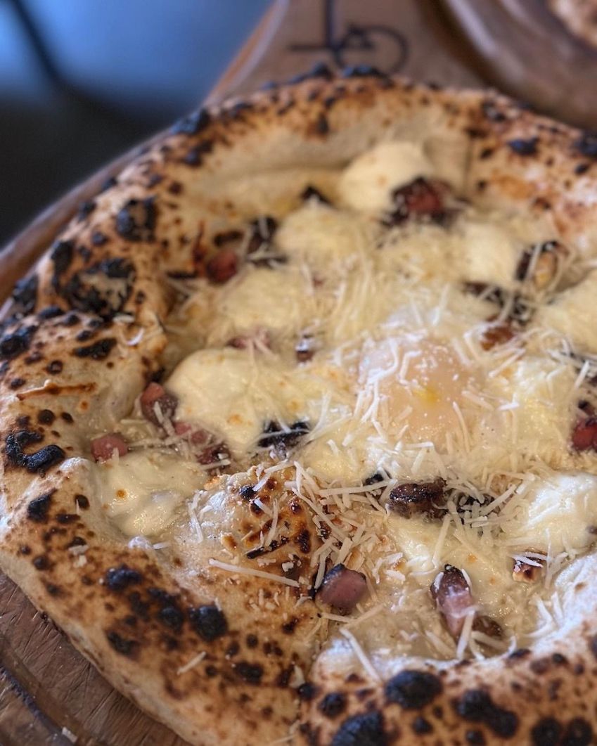 Pizza "Carbonara" coberta de muçarela fior di latte, queijo parmesão, ovo de gema mole e guanciale / Tina Bini