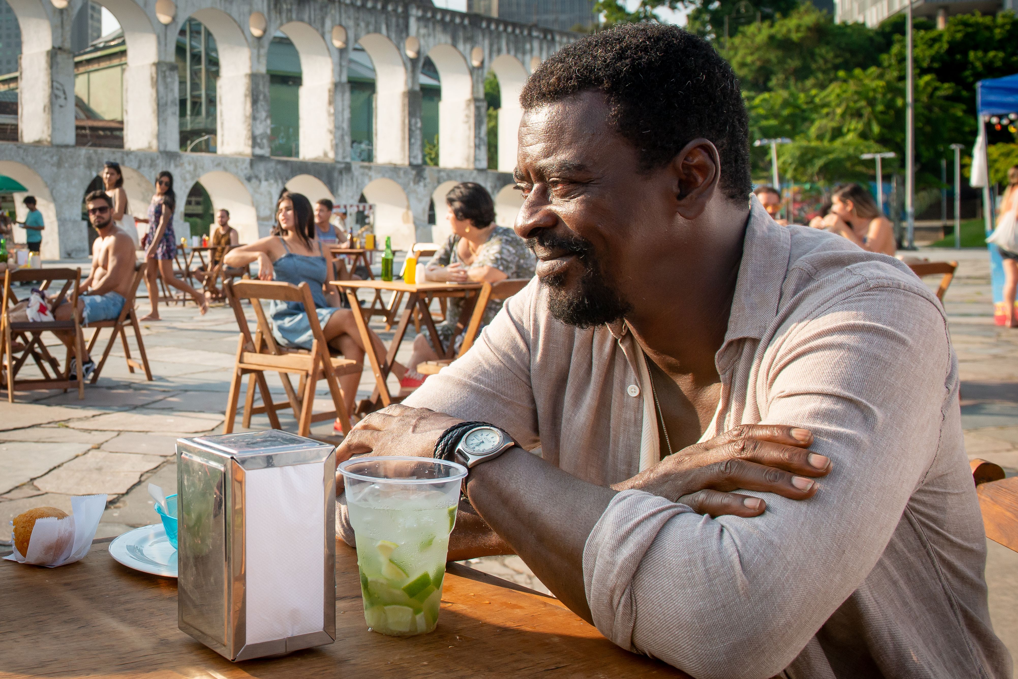 Seu Jorge em cena de How To Be a Carioca com os Arcos da Lapa ao fundo