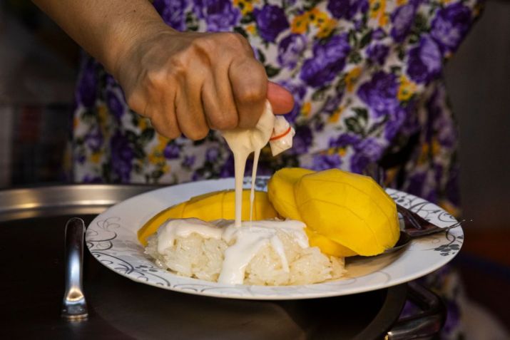 Uma vendedora coloca creme de coco em cima do arroz da sobremesa / Lauren DeCicca/Getty Images