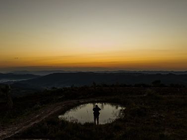 Homem parado em frente a pequeno lago no entardecer