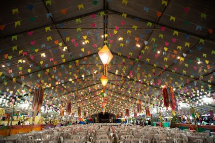 Galpão repleto de cadeiras e bandeirinhas juninas no Arraial Gastronômico do Projeto Buscapé