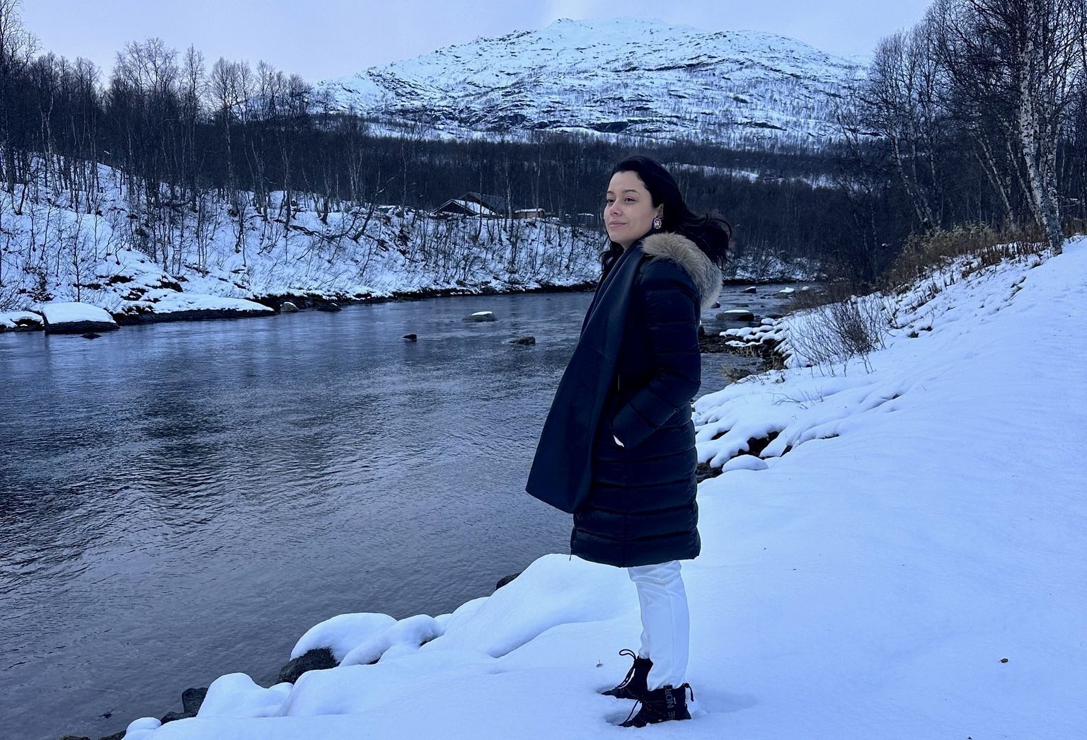 Daniela Filomeno de frente para rio e paisagens com gelo na Lapônia Norueguesa