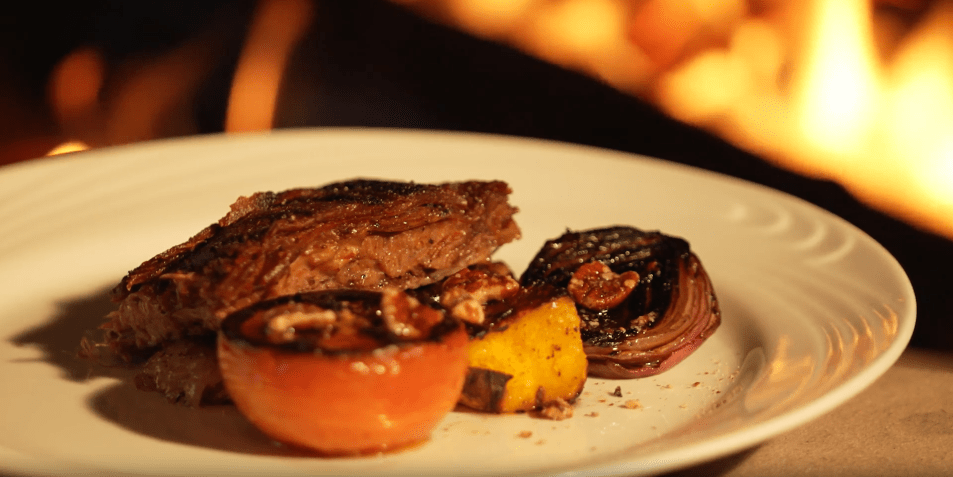 Costelão de angus feito no fogo de chão servido com cebola, tomate e noz-pecã • CNN Viagem & Gastronomia