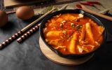 A horizontal shot of a soup in black bowl and some eggs and wooden chopsticks