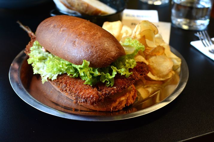Sanduíche de peixe à milanesa com picles de cebola, maionese e alface em pão brioche, acompanhado de batatas chips • Giuliana Nogueira