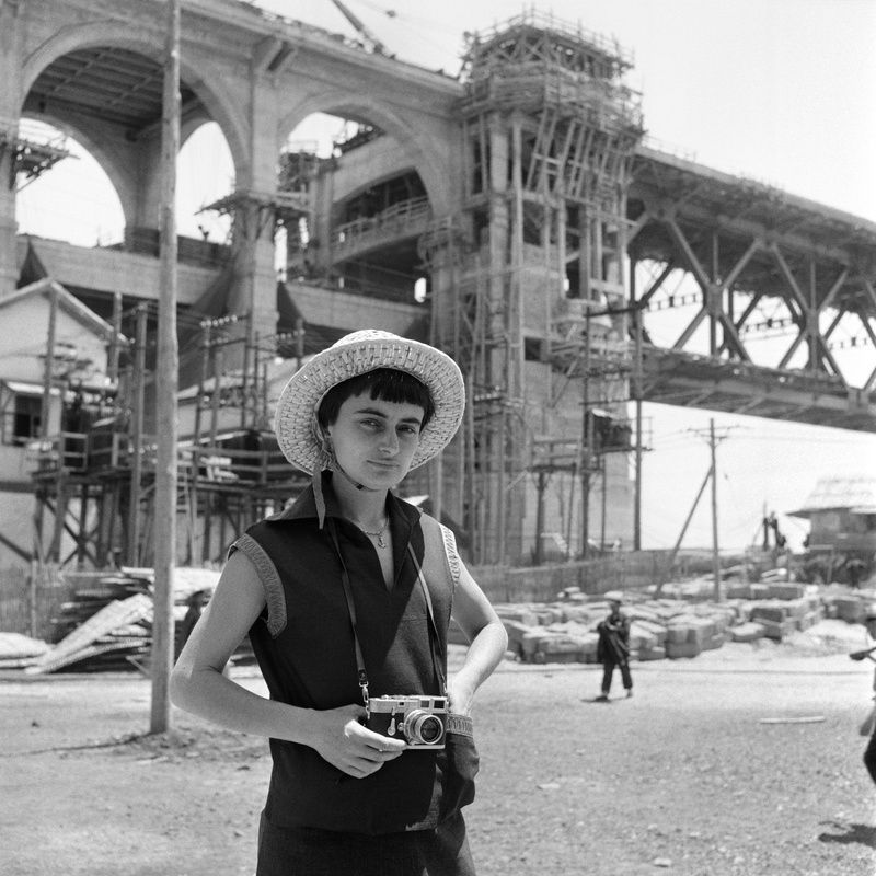 Agnès Varda com sua câmera Leica na frente da ponte de Wuhan em construção, China, 1957 • Arquivo Agnés Varda