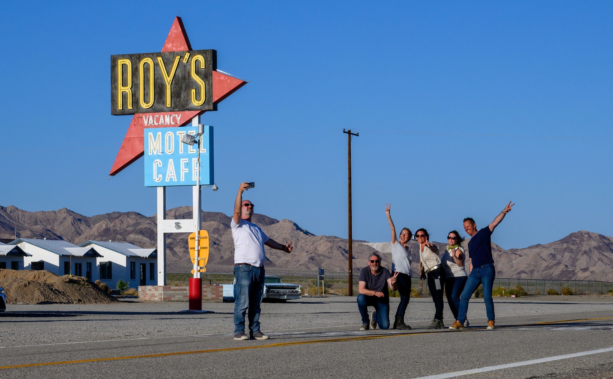 Turistas franceses tiram uma selfie em grupo em frente à placa do Roy's Motel & Cafe em 24 de maio de 2024, em Amboy, Califórnia • Gina Ferazzi/Los Angeles Times/Getty Images via CNN Newsource