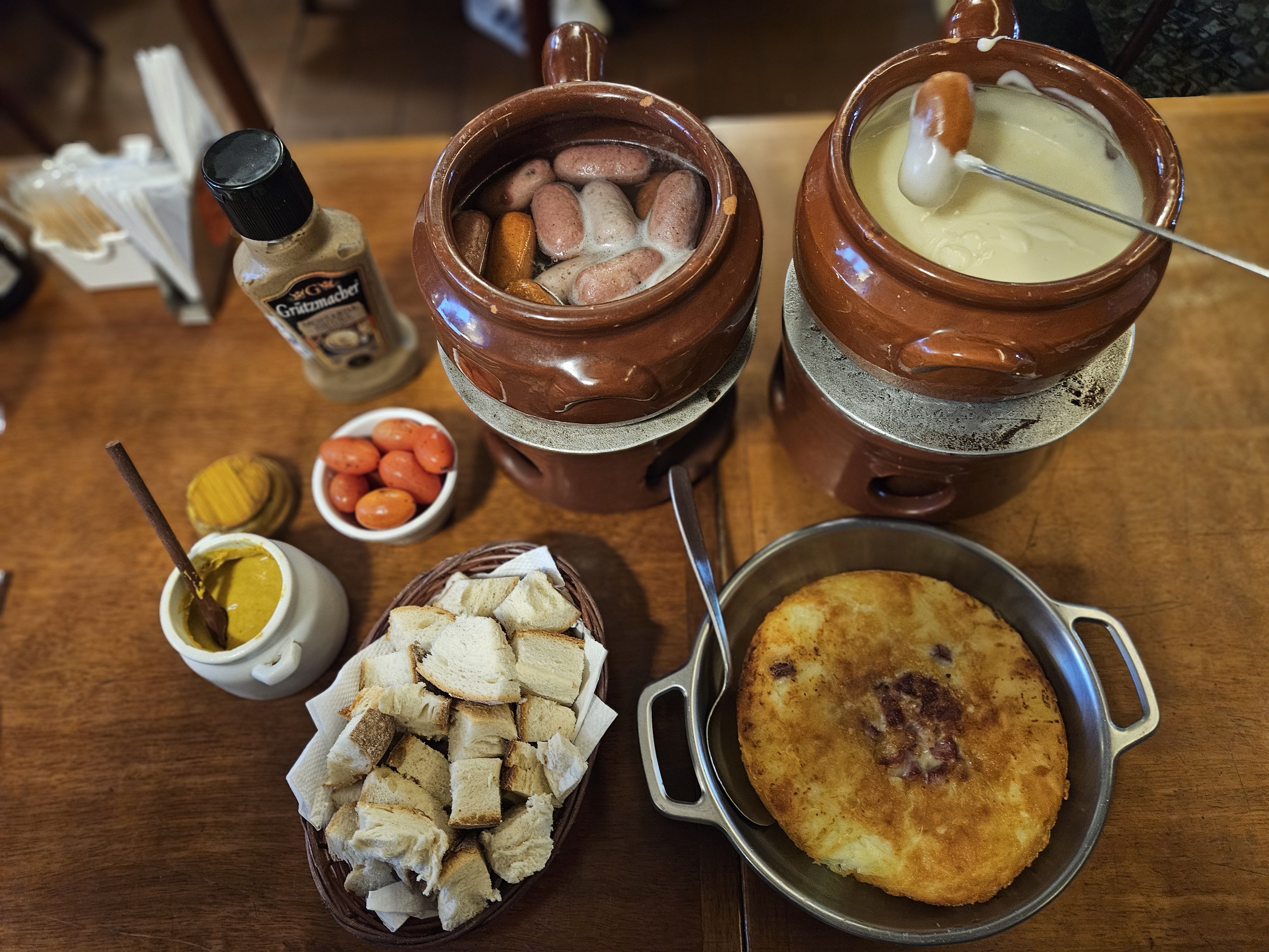 O fondue de queijo chega acompanhado de minisalsichas, pão italiano, tomate-cereja e mostarda. Ainda é possível acrescentar batata rösti • Divulgação