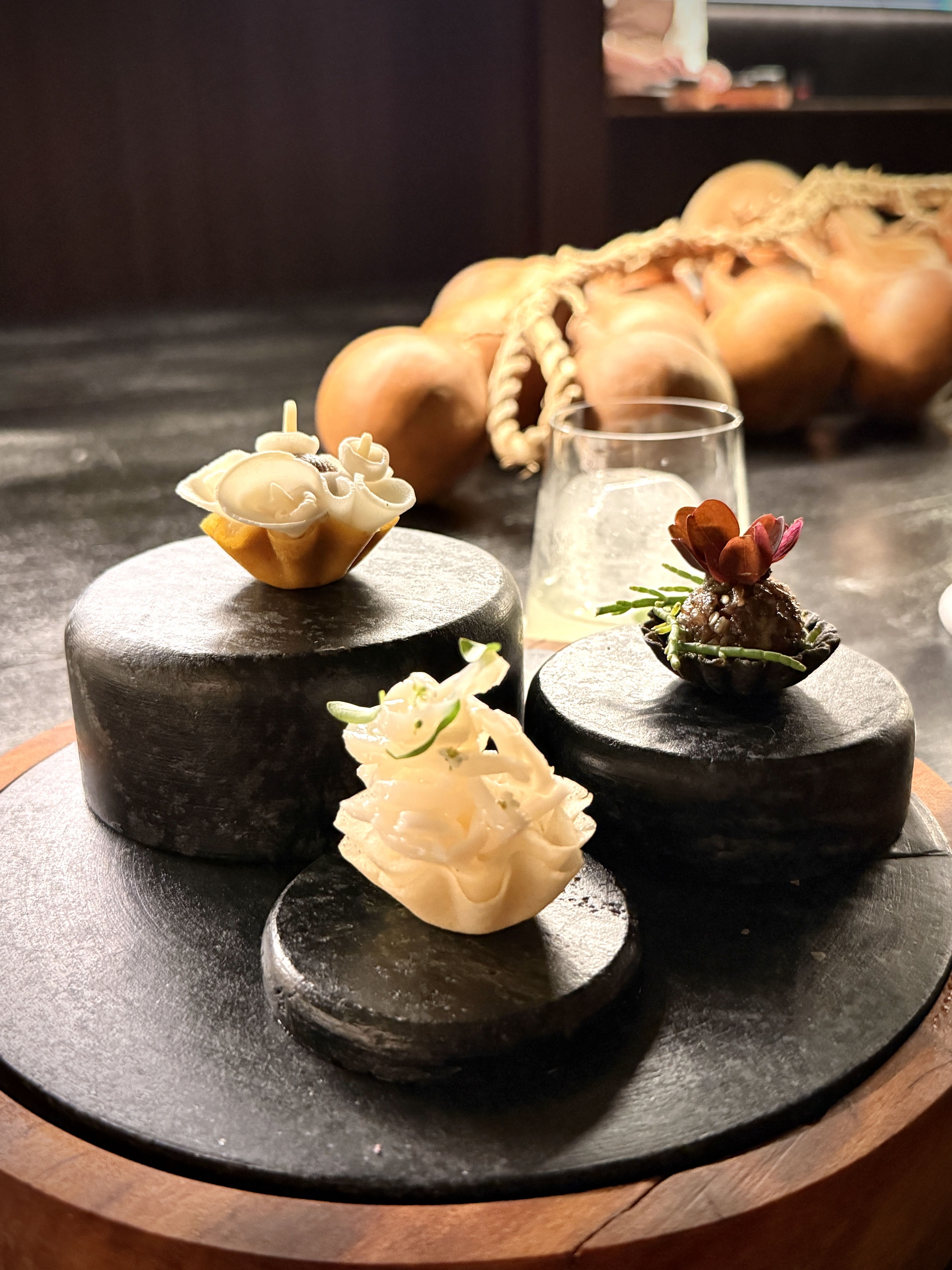 Coco verde com lula, carvão com abacate e Denver e pupunha com enoki e castanha aparecem entre os amuse-bouche, em delicadas criações que dão início à jornada no Dêze e já revelam a presença de frutas e brasilidades ao longo da noite • Tina Bini