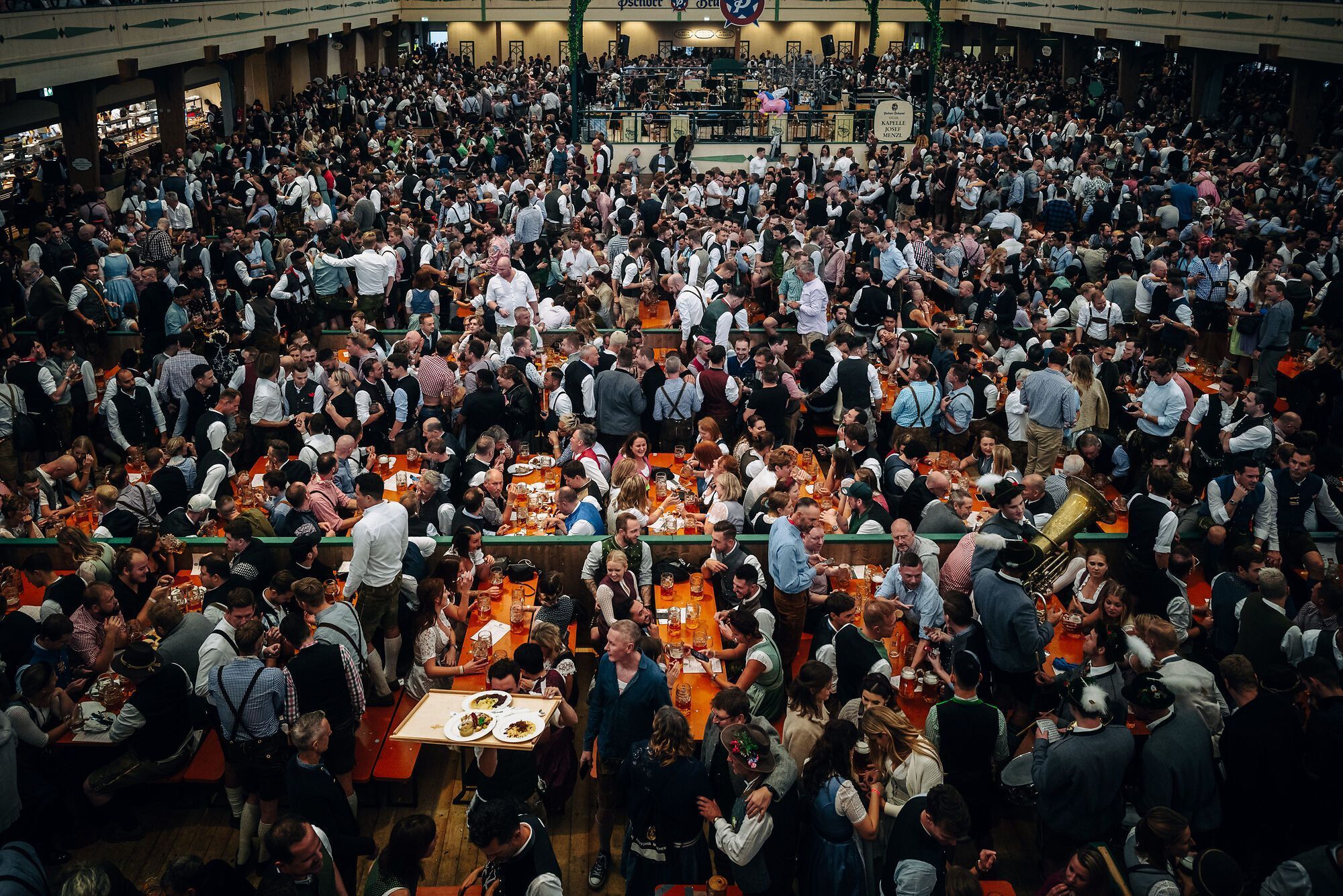 Interior de uma das tendas da Oktoberfest, com mesas lotadas e música ao vivo • © München Tourismus Jan Saurer